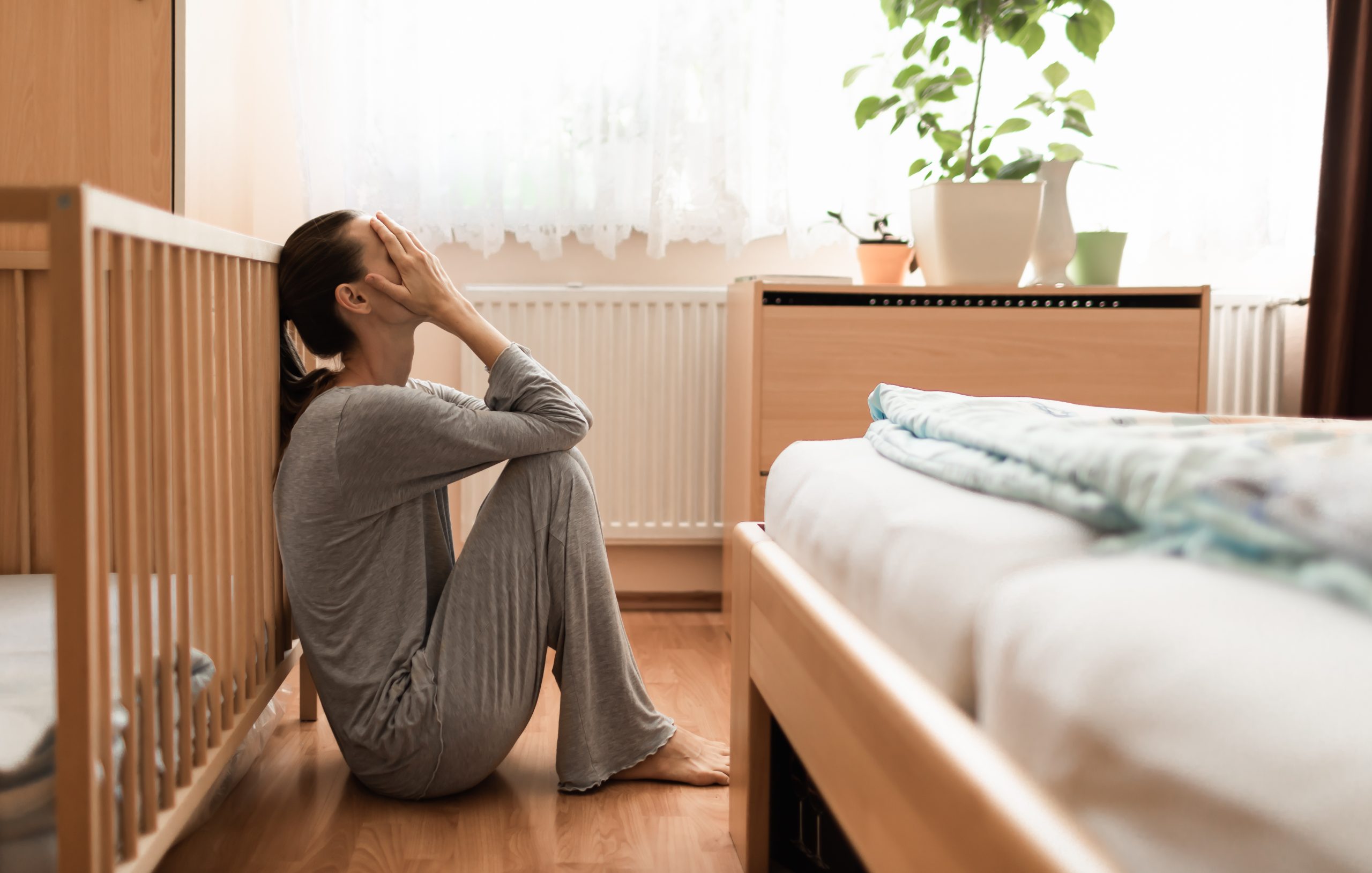 tired mom sitting on the floor by the cot with head in hands