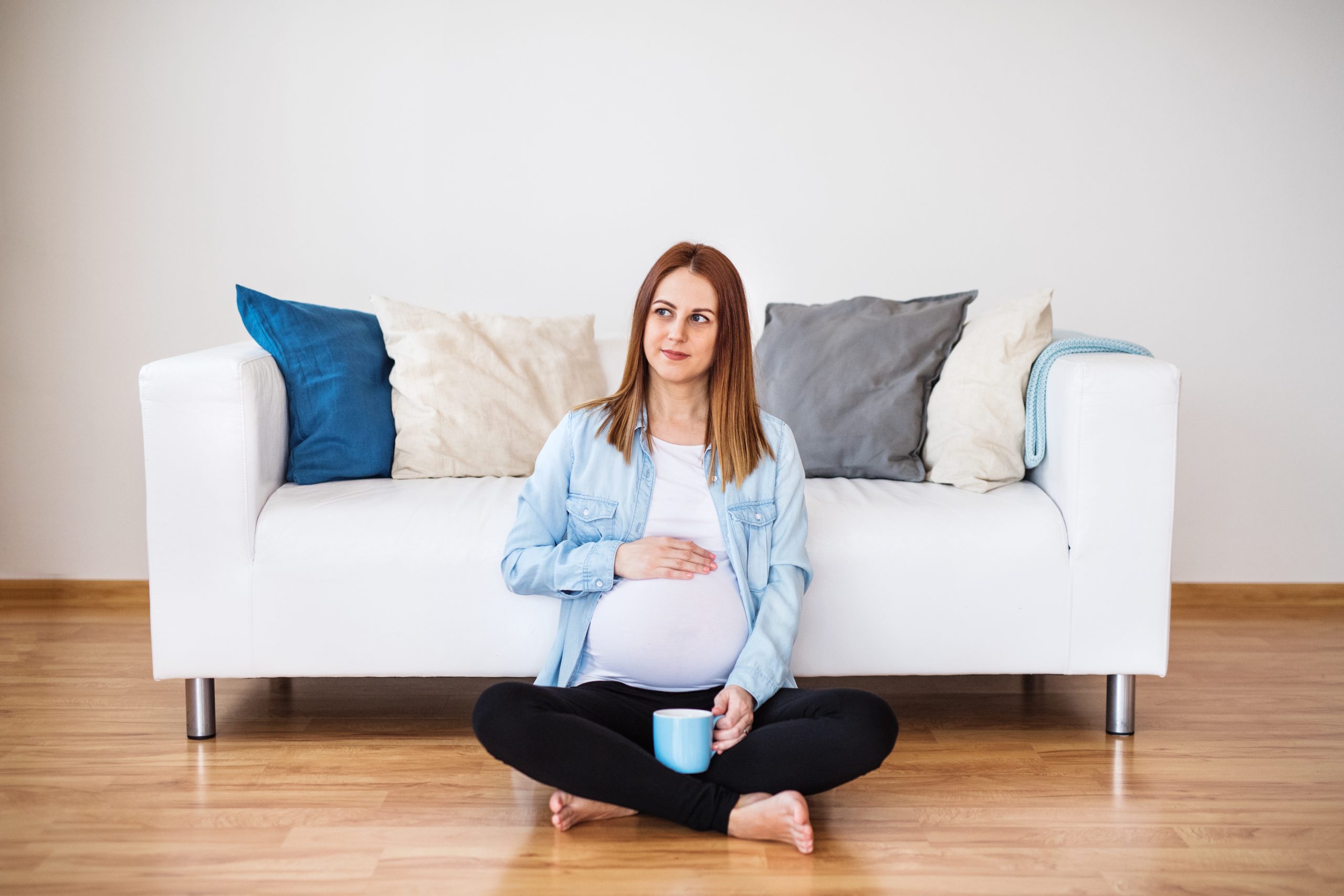 Pregnant woman sitting on floor, drinking tea. 