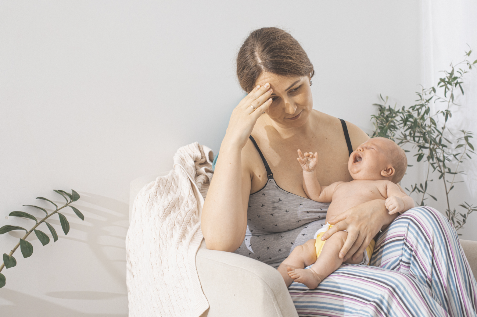 new mother breastfeeding baby with sad and tired look on face