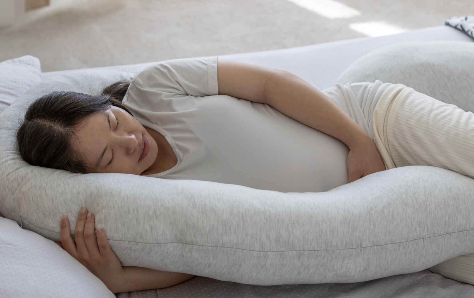 pregnant woman laying down on bed with pregnancy pillow