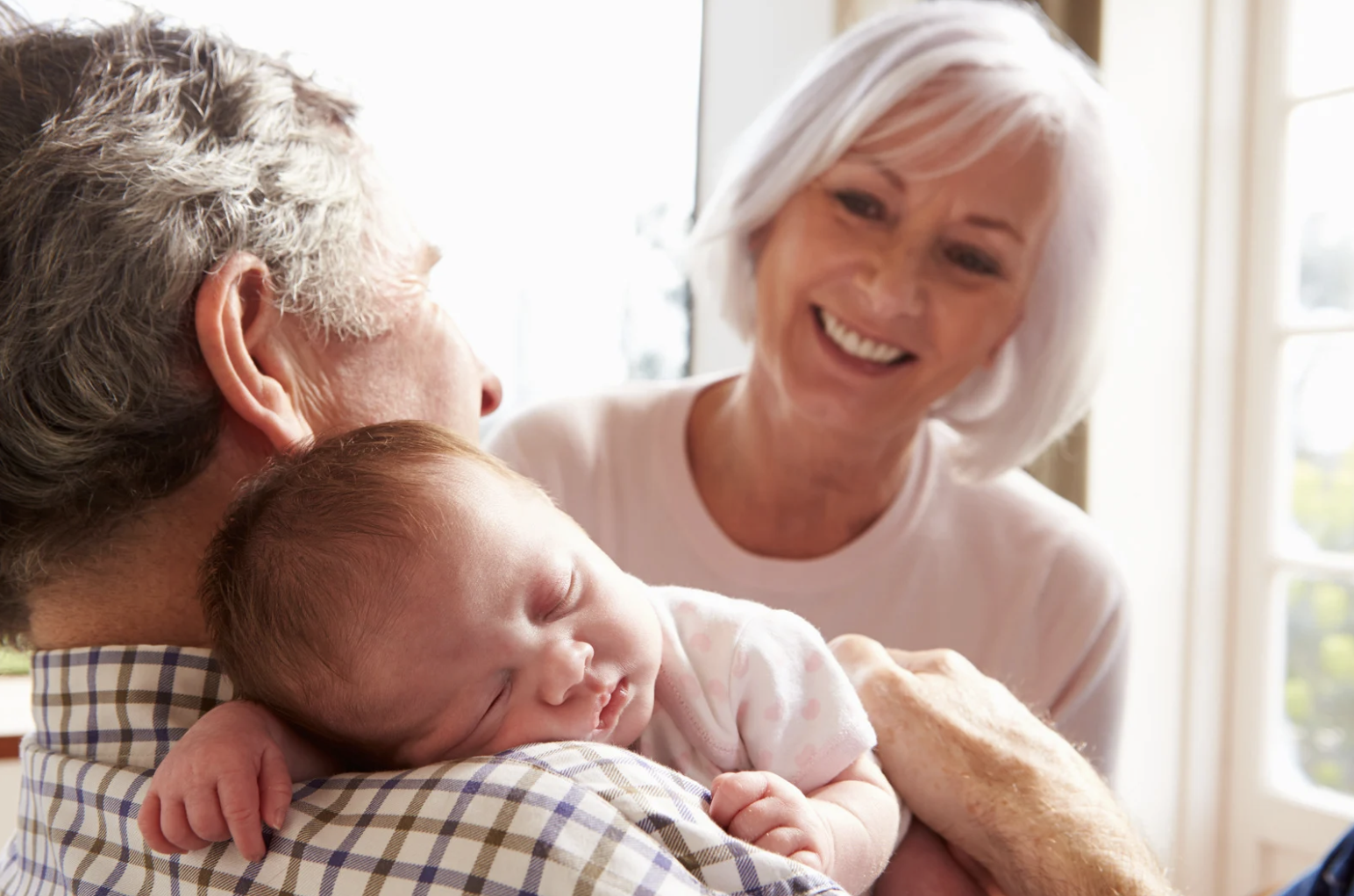 Grandparents smiling and holding newborn baby at home