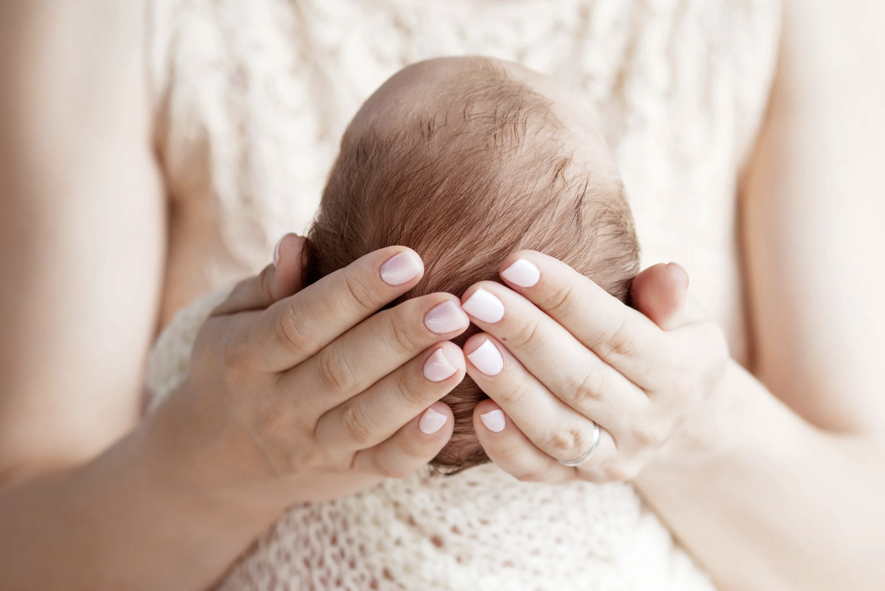 Newborn baby being gently cradled in parent’s hands