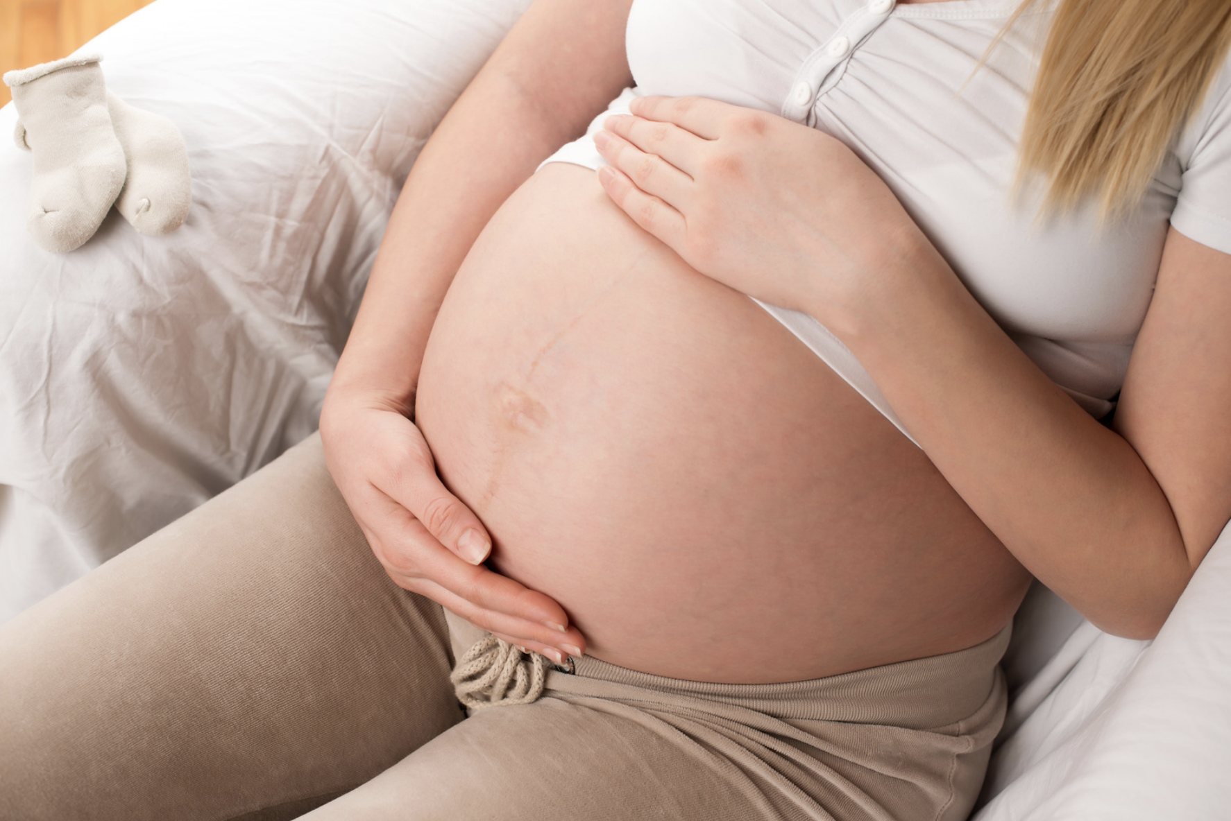 Pregnant woman gently holding her bump while resting on a bed