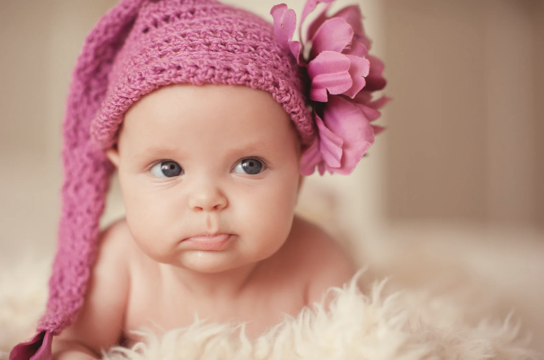 baby girl wearing a pink knitted hat with flower detail, lying on a fluffy blanket